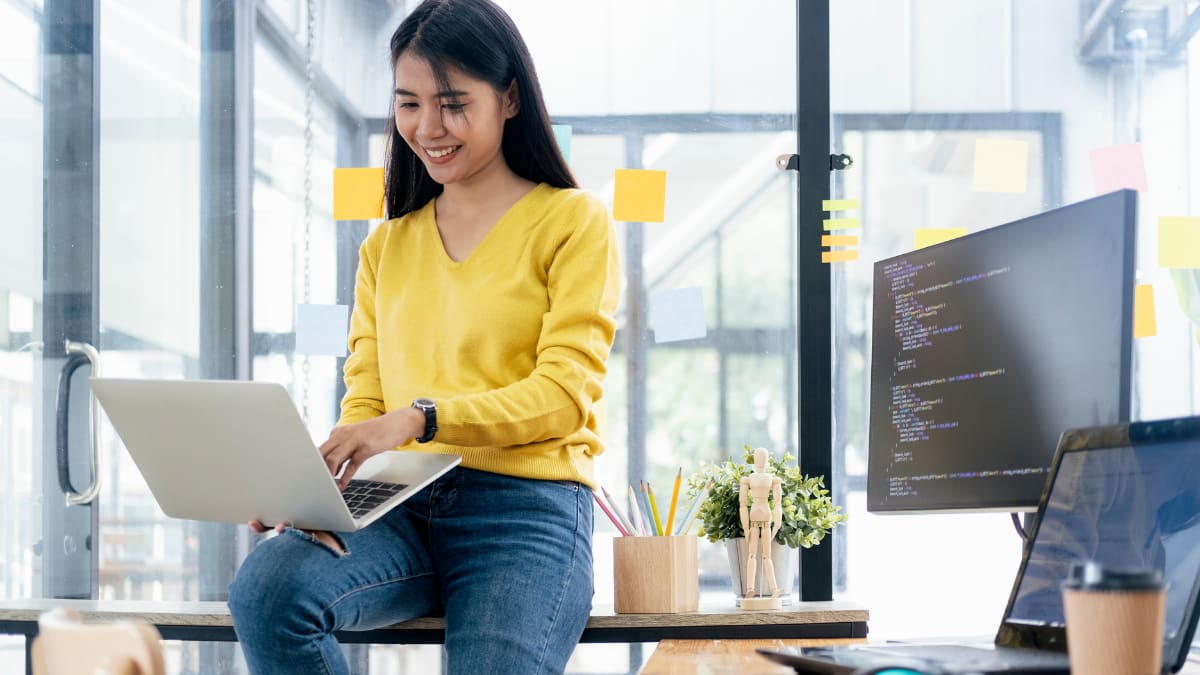 cybersecurity professional sitting on a desk holding a laptop