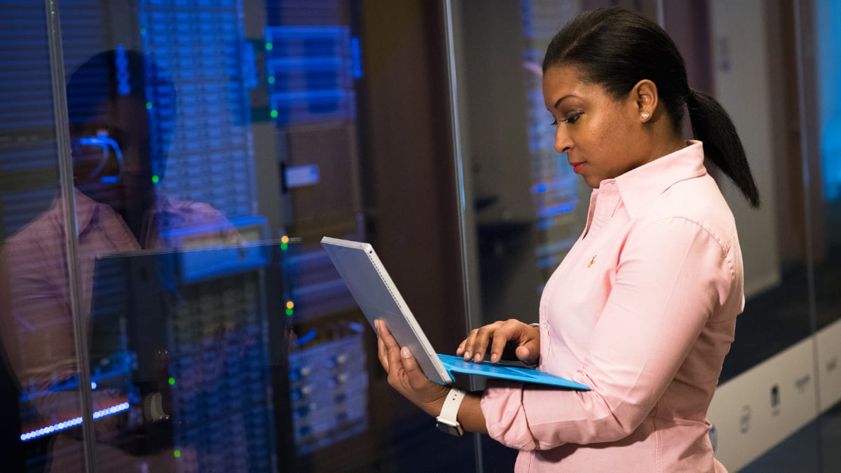 cyber security expert standing in a server room and holding a laptop