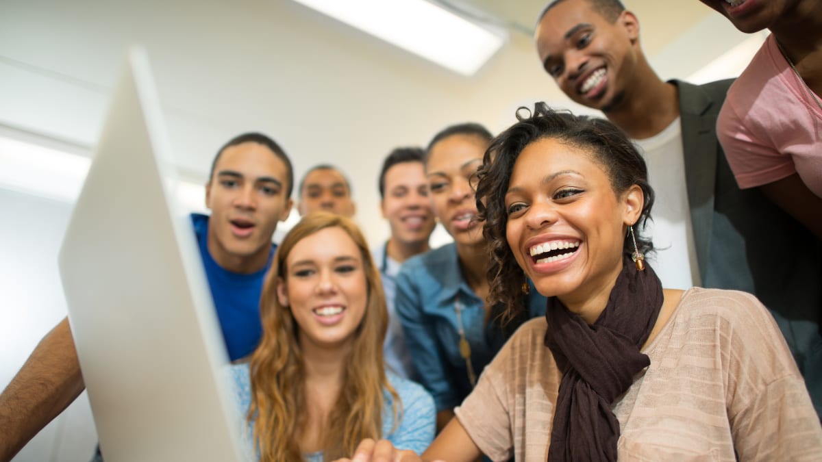 smiling college students sitting around a laptop computer