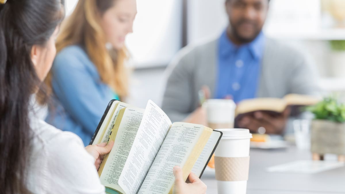 three students looking at the Bible together while sitting around a table