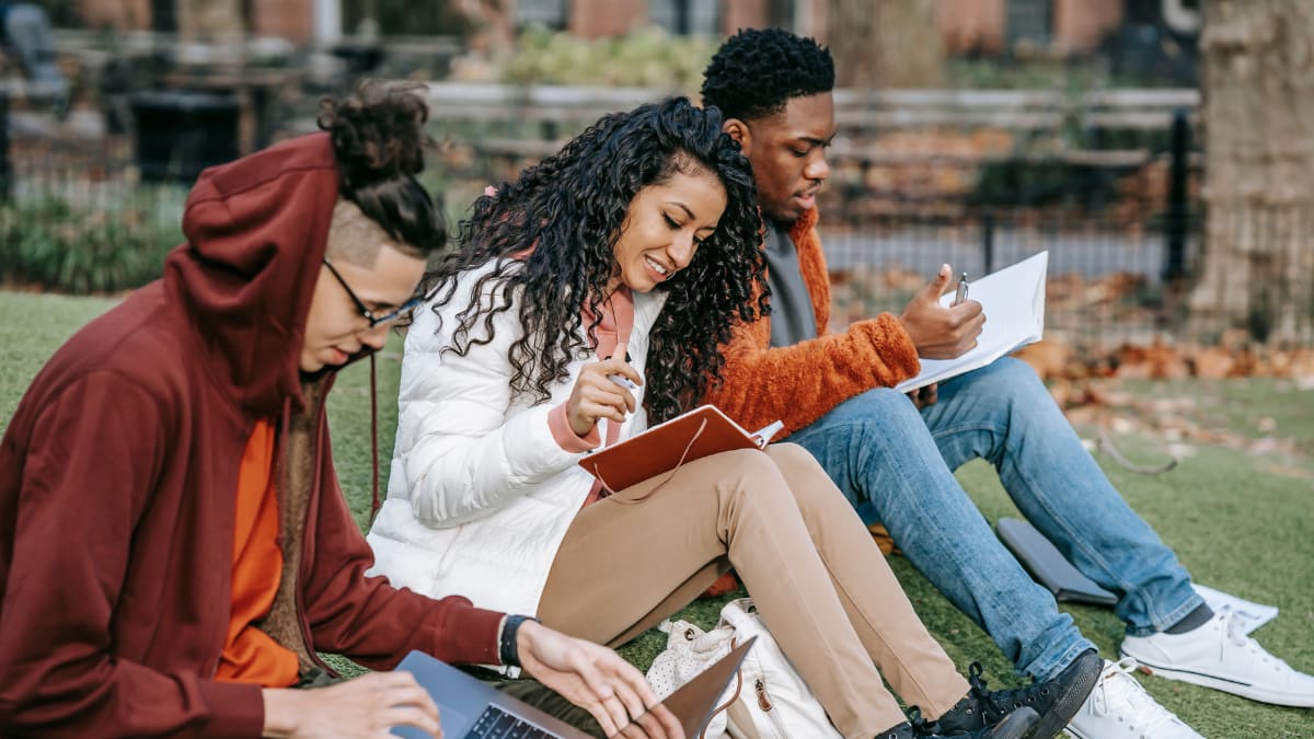 three college students sitting together on the grass studying