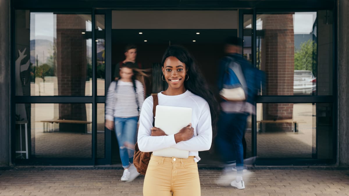 college student standing outside a building with other students exiting the building in the background