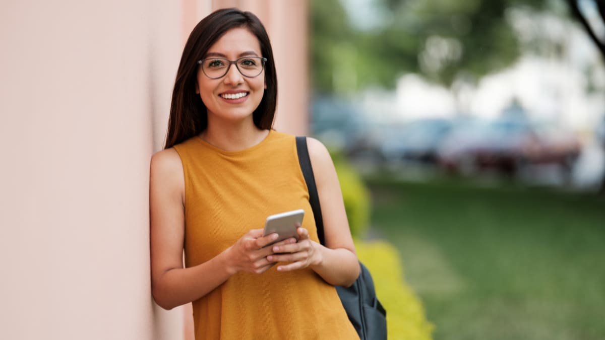 college student leaning against a wall while holding a cell phone