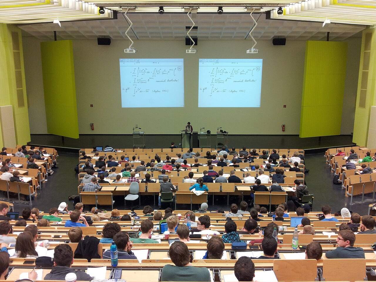 Students sitting in a lecture hall with a professor projecting lesson notes on the wall