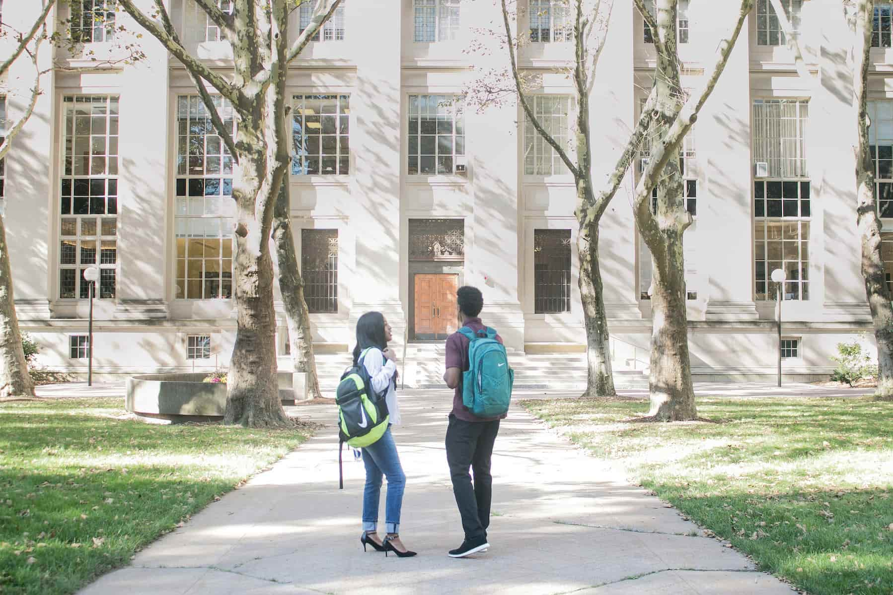 Two students walking on a concrete path on their way to their school building