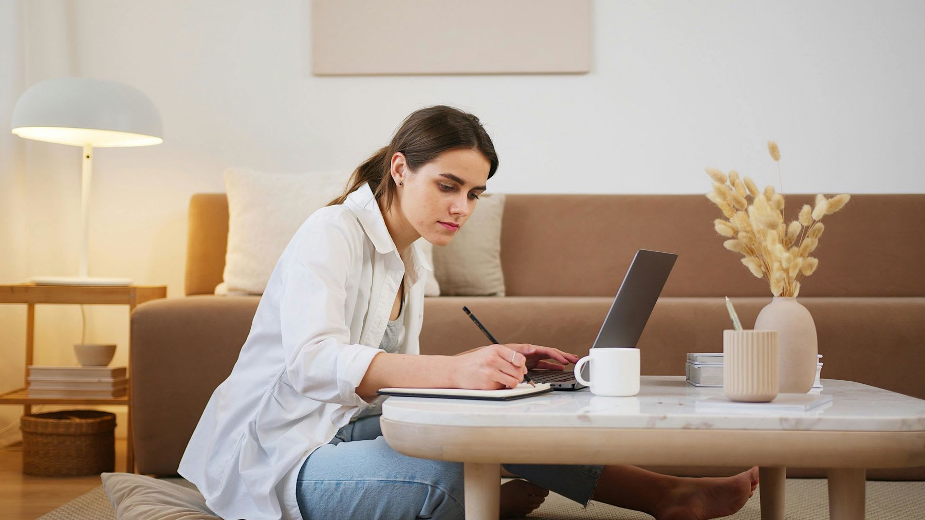 Woman sitting on the floor while taking notes and using her laptop