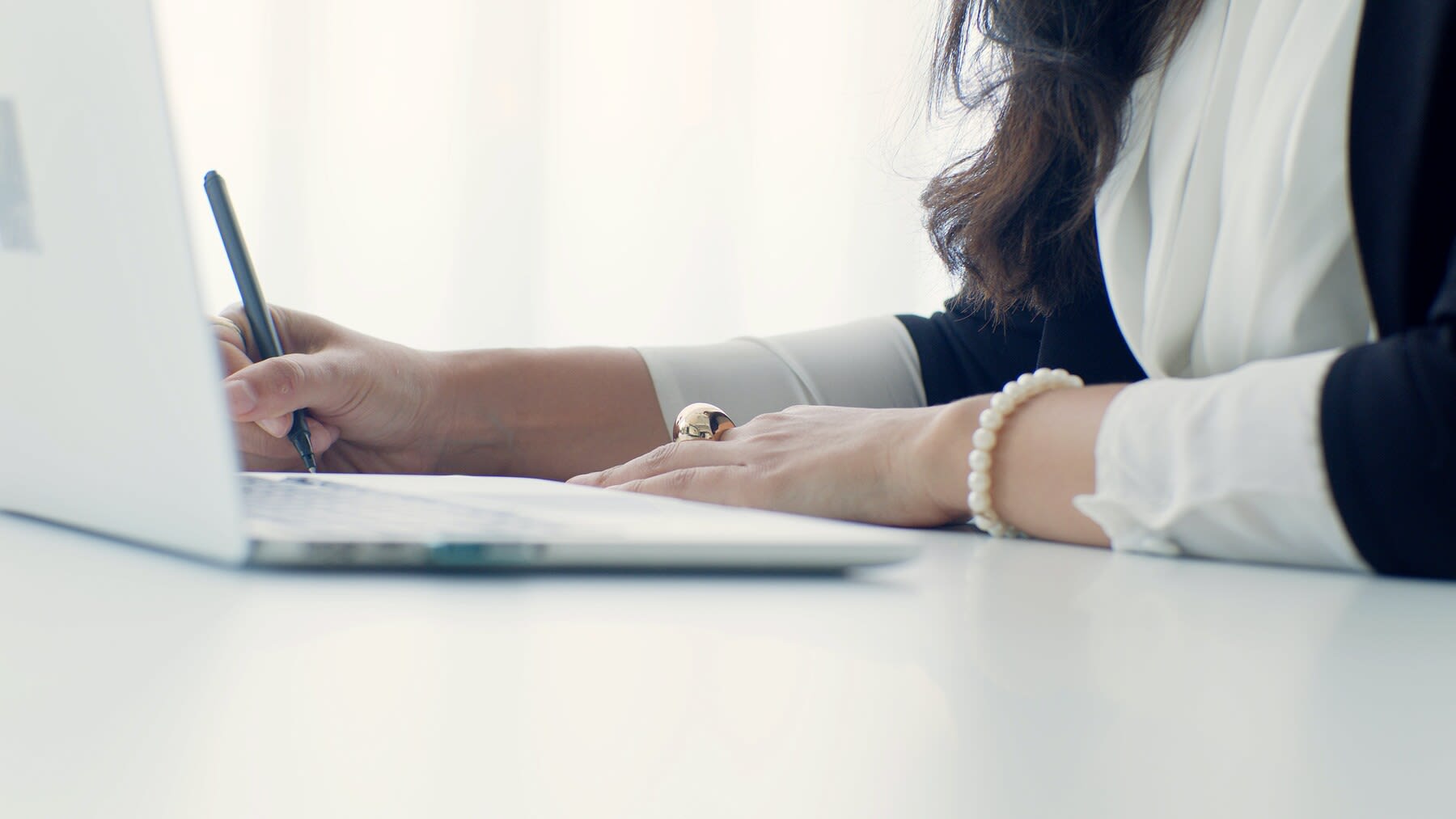 Woman writing while looking at her laptop