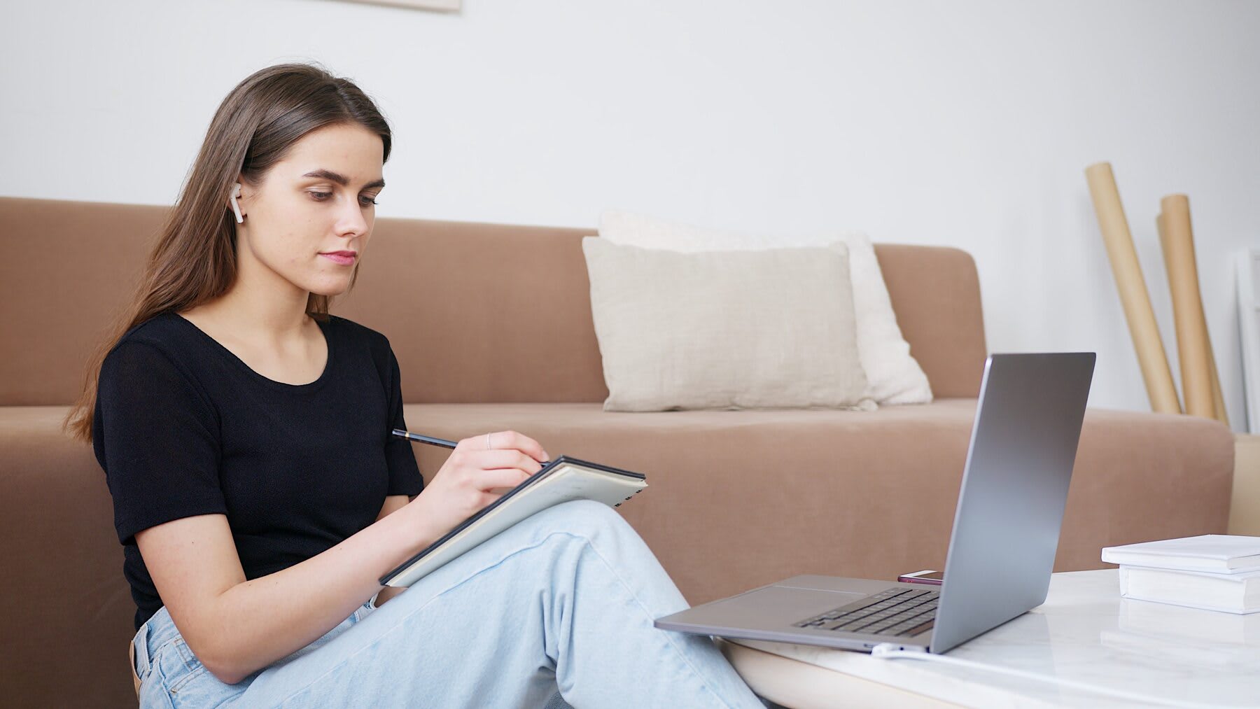 Woman writing on her notebook while looking at her laptop