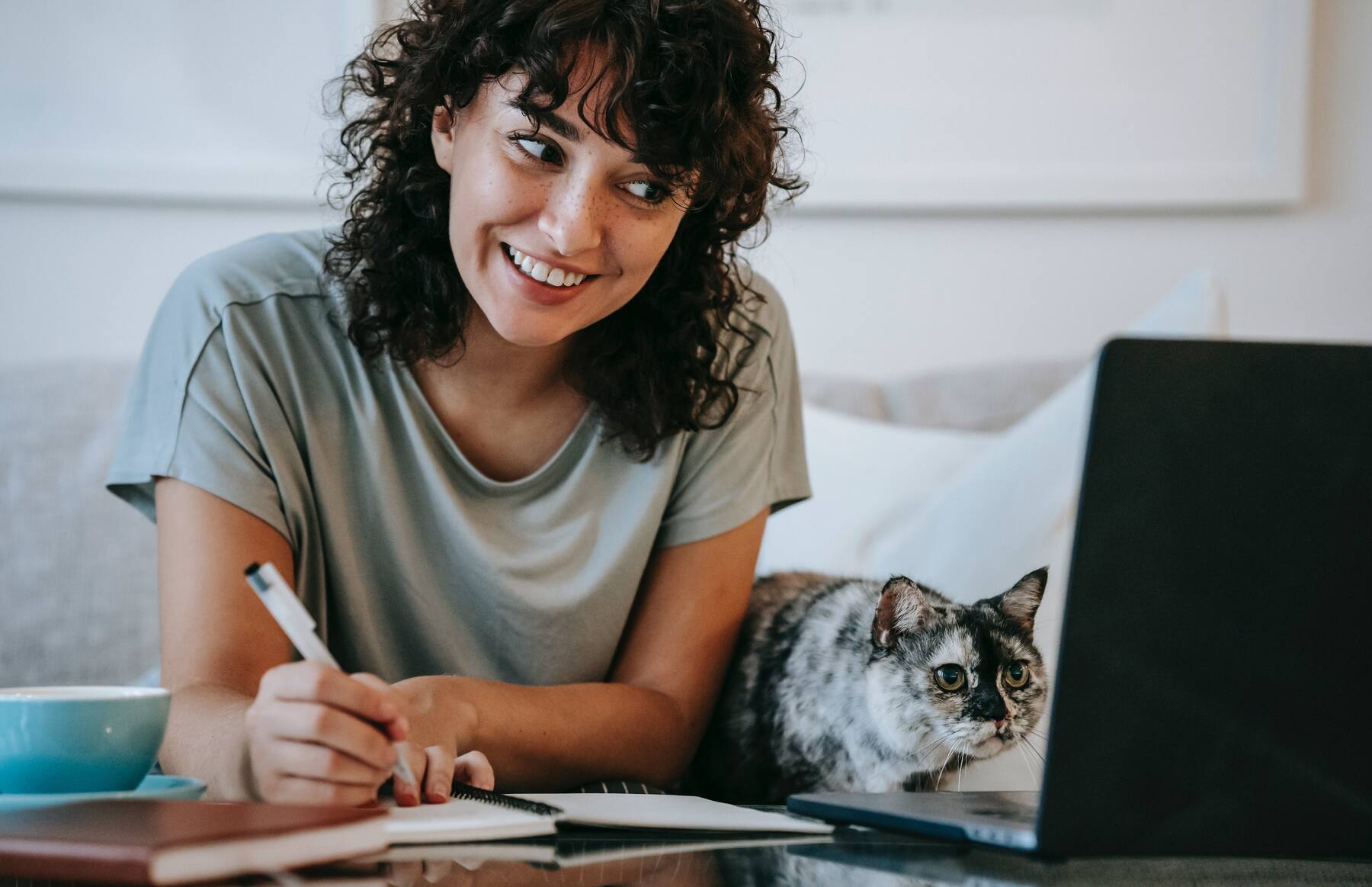 Woman writing on a notebook while looking at a laptop