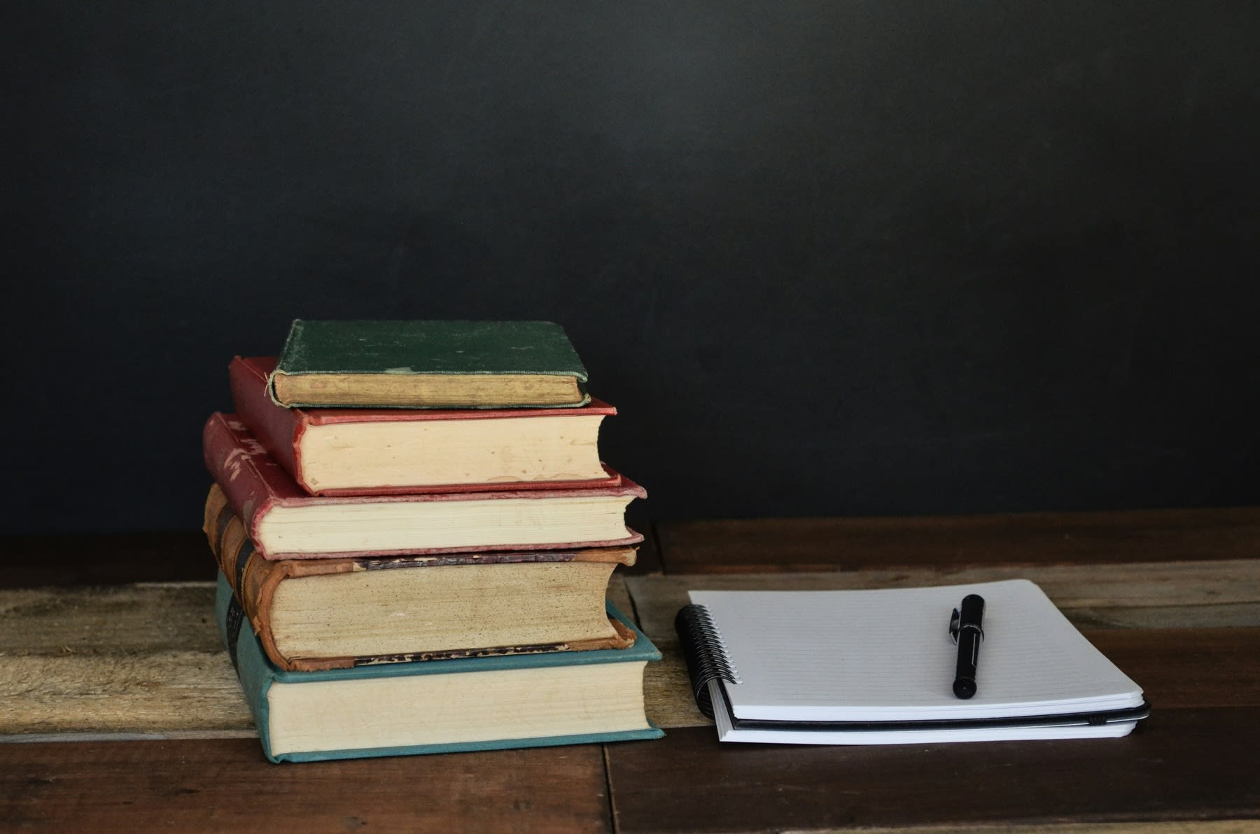 Stack of books and a notebook with a pen, all placed in one table