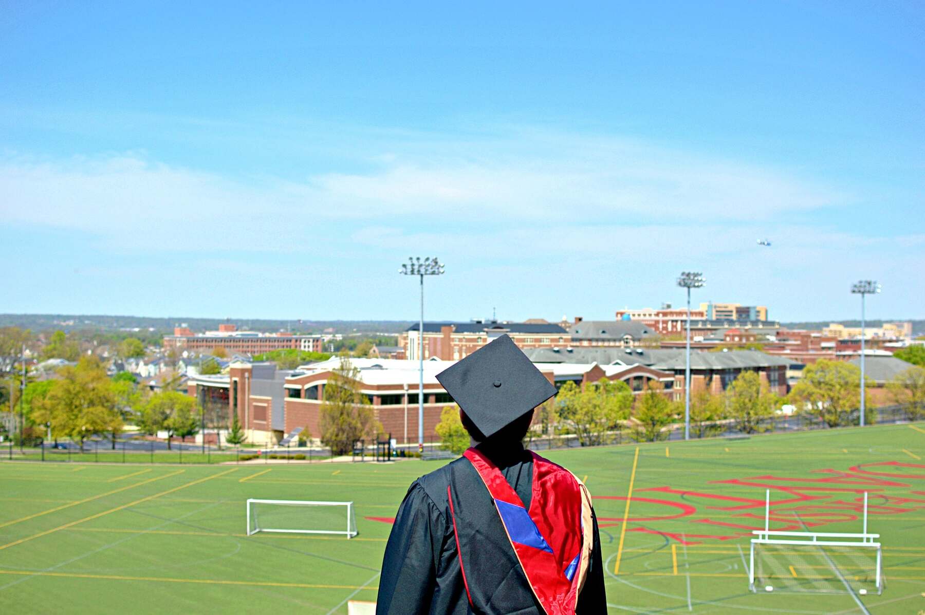 Man wearing graduation robes while looking at a sports field