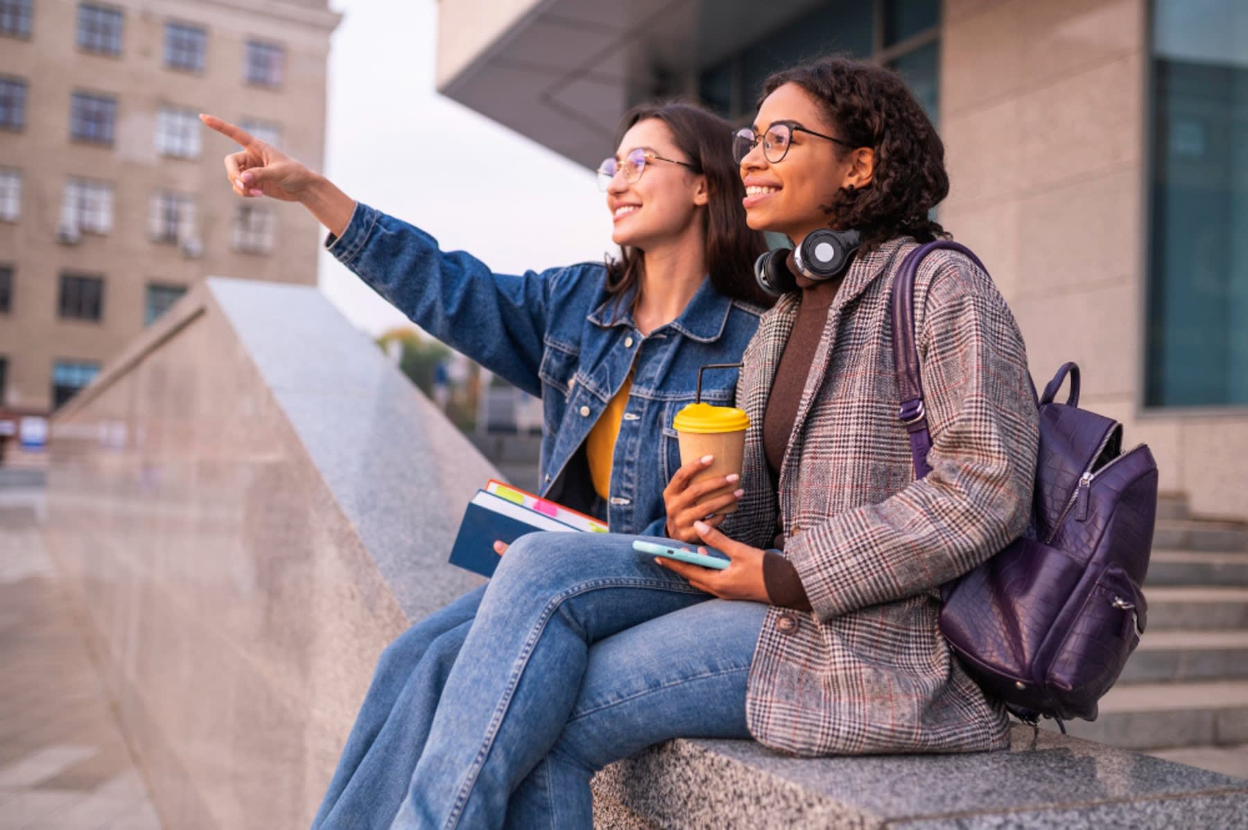 Two female students sitting near the stairs while looking and pointing overhead