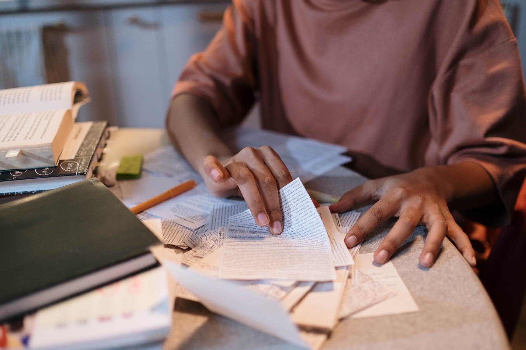 Woman looking through her notes on a cluttered table with several books and papers on it