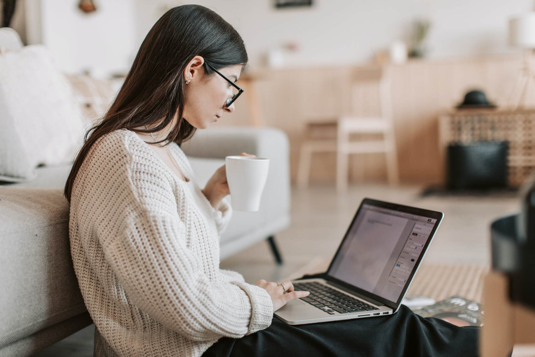 Woman holding a cup of coffee while browsing in her laptop