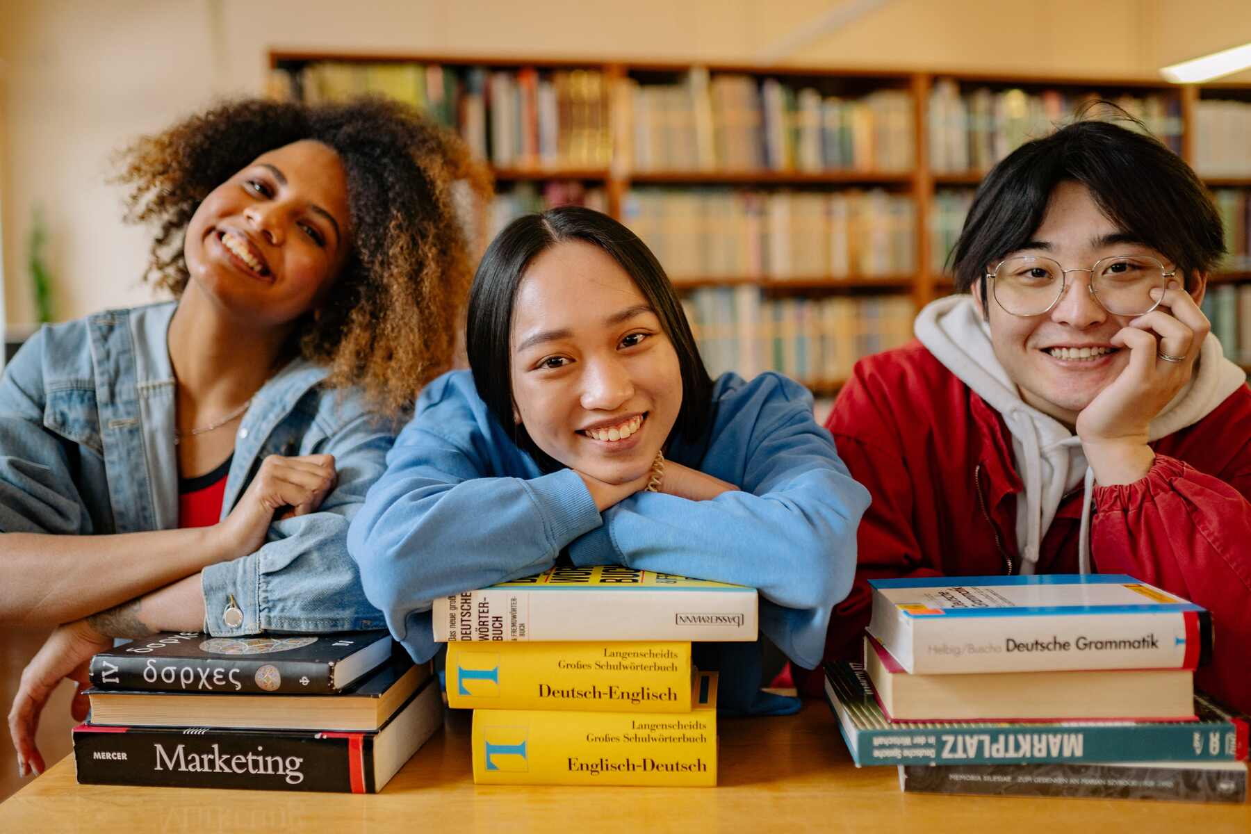 Three international students with piles of books in front of them