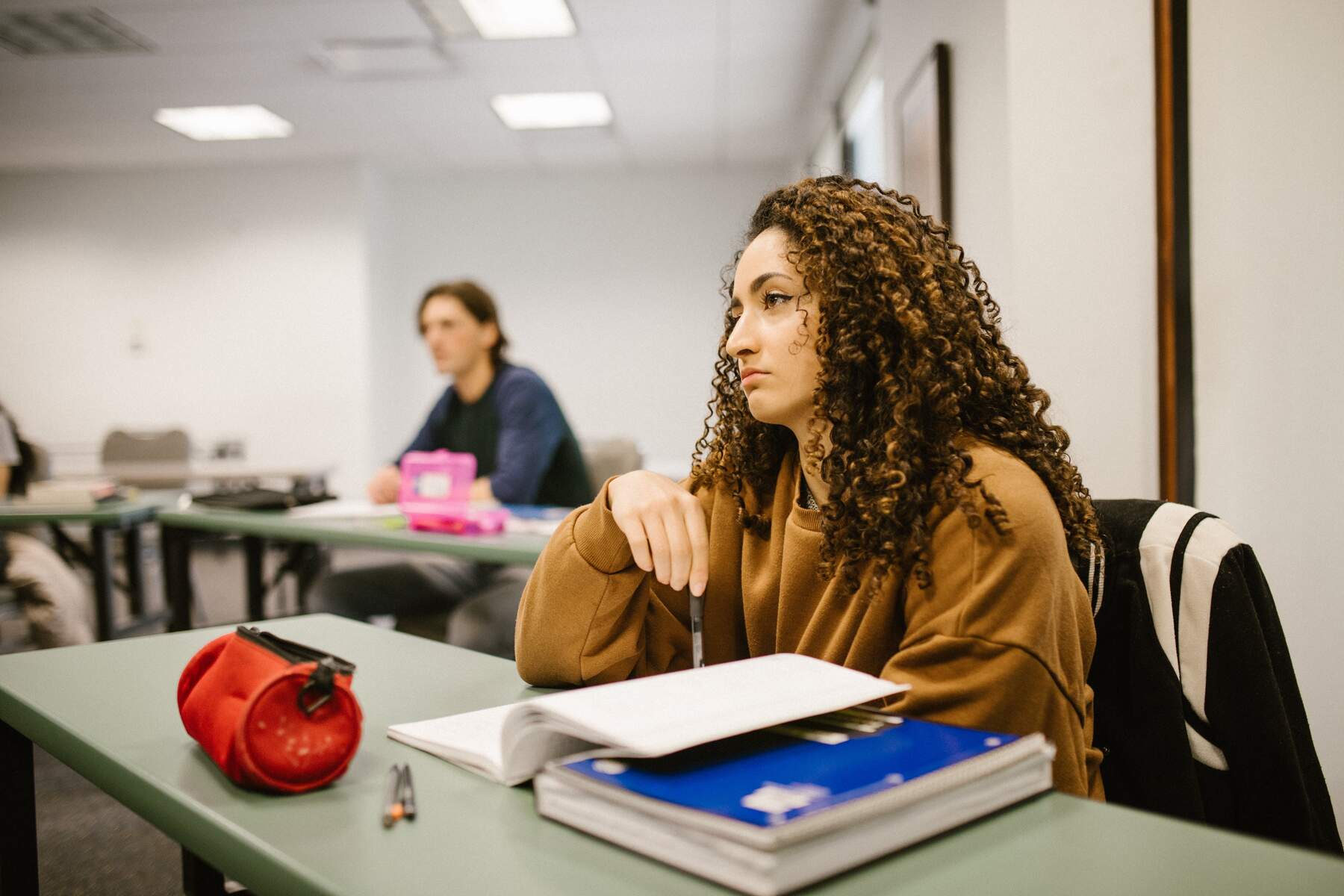 Woman with her notebook and pen ready, sitting in a classroom and listening to a lecture