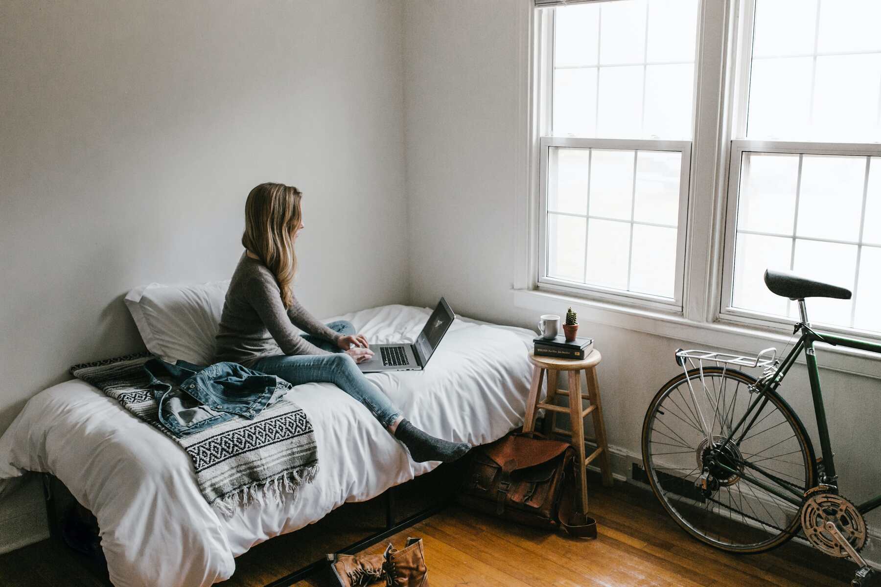 Woman using her laptop while sitting on her bed