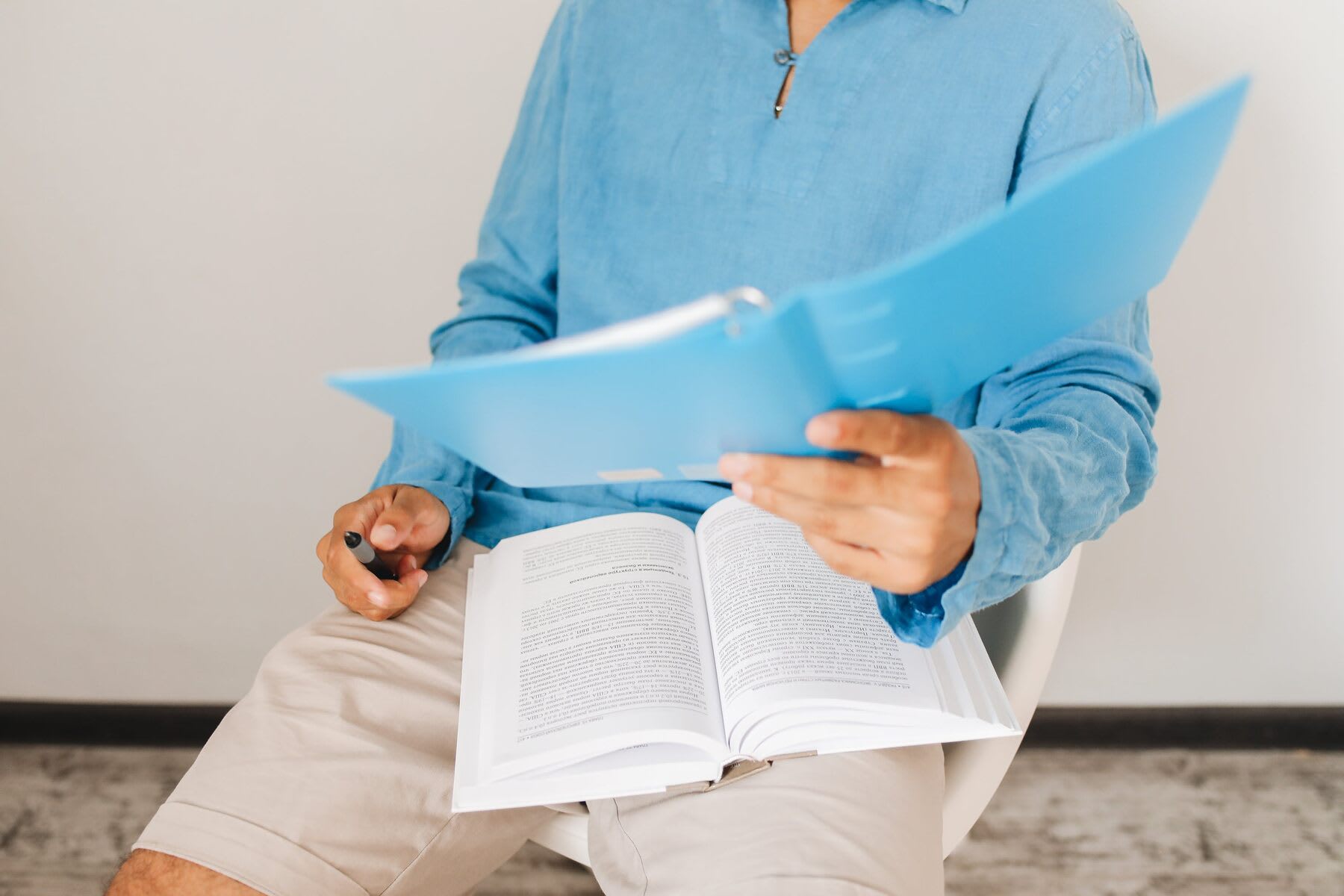 Man reading a blue folder while a text book is on his lap