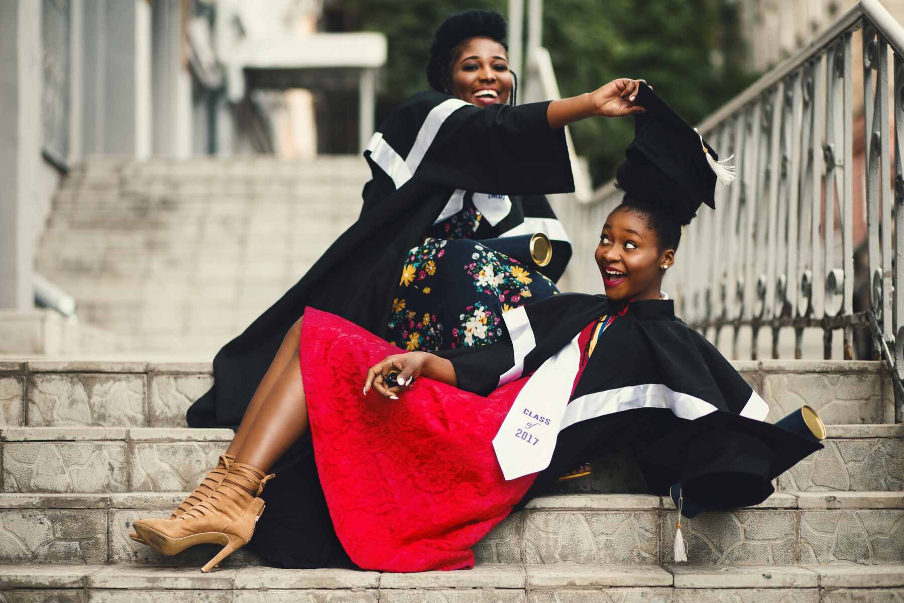 Two girls sitting on the school steps and playing with their graduation robes