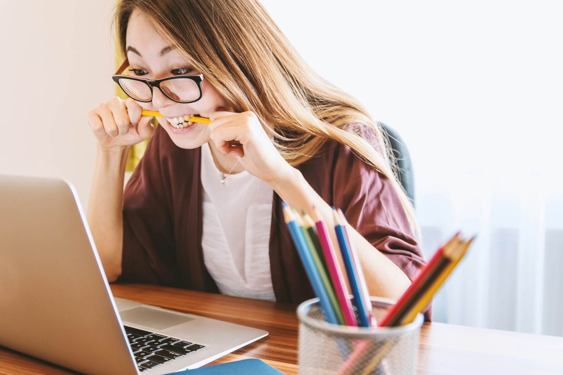 Woman biting her pencil while staring at her laptop screen