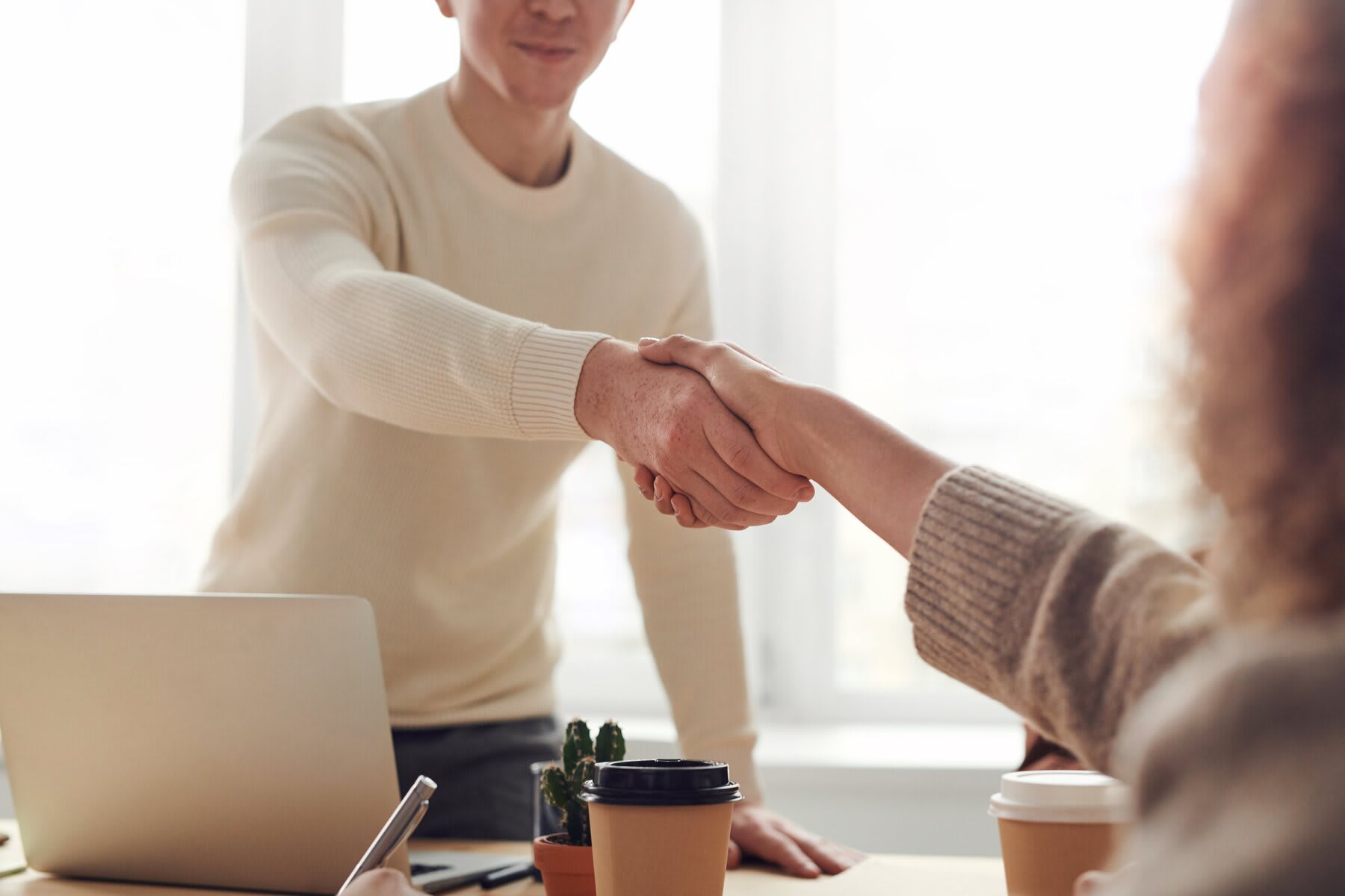 Man getting up from his seat while shaking hands with a woman in front of him