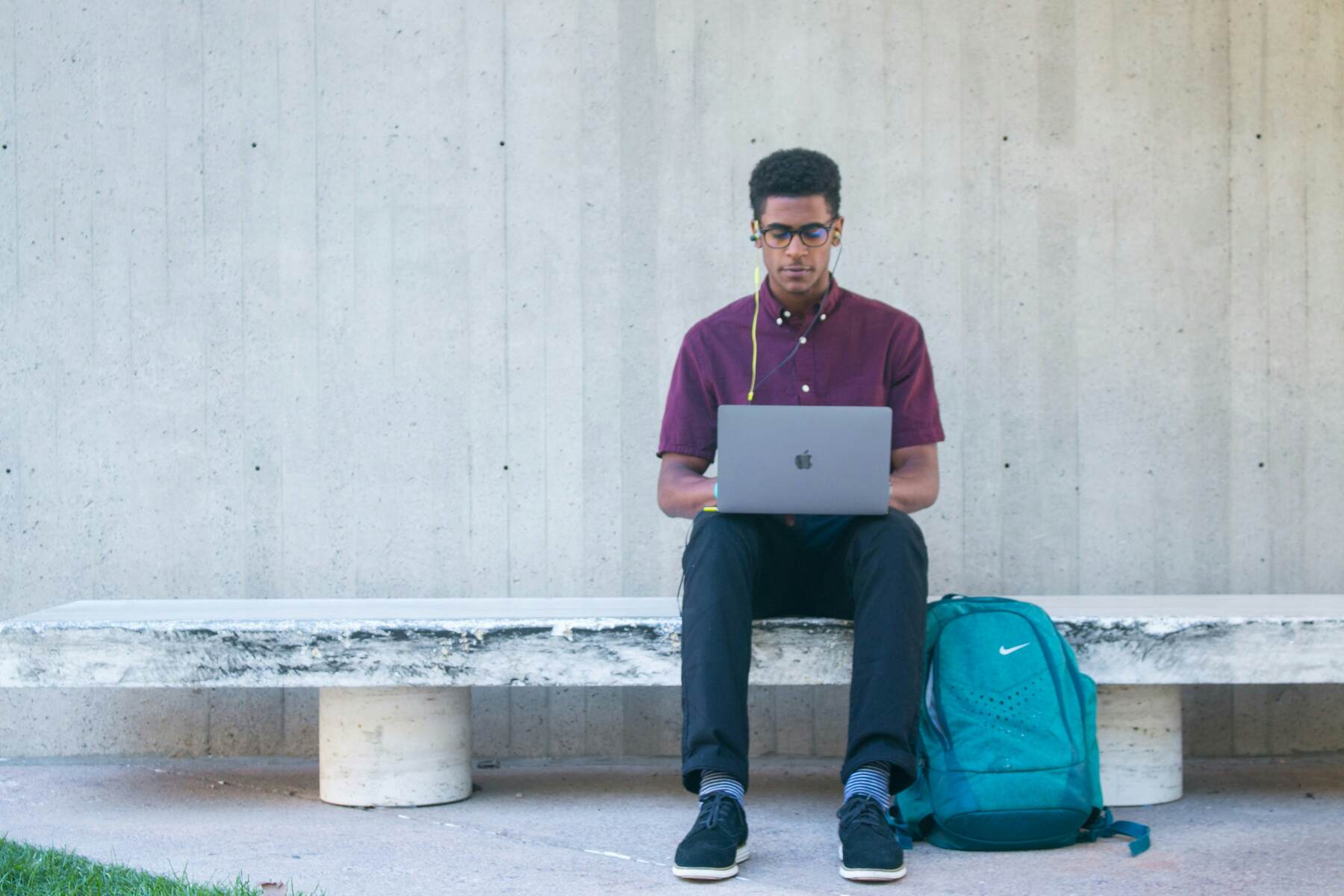 Man sitting on an outdoor bench while using his laptop