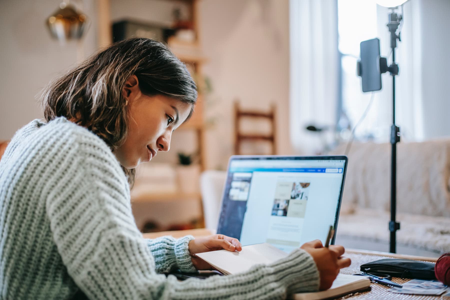 Woman writing on her notebook while her laptop is open