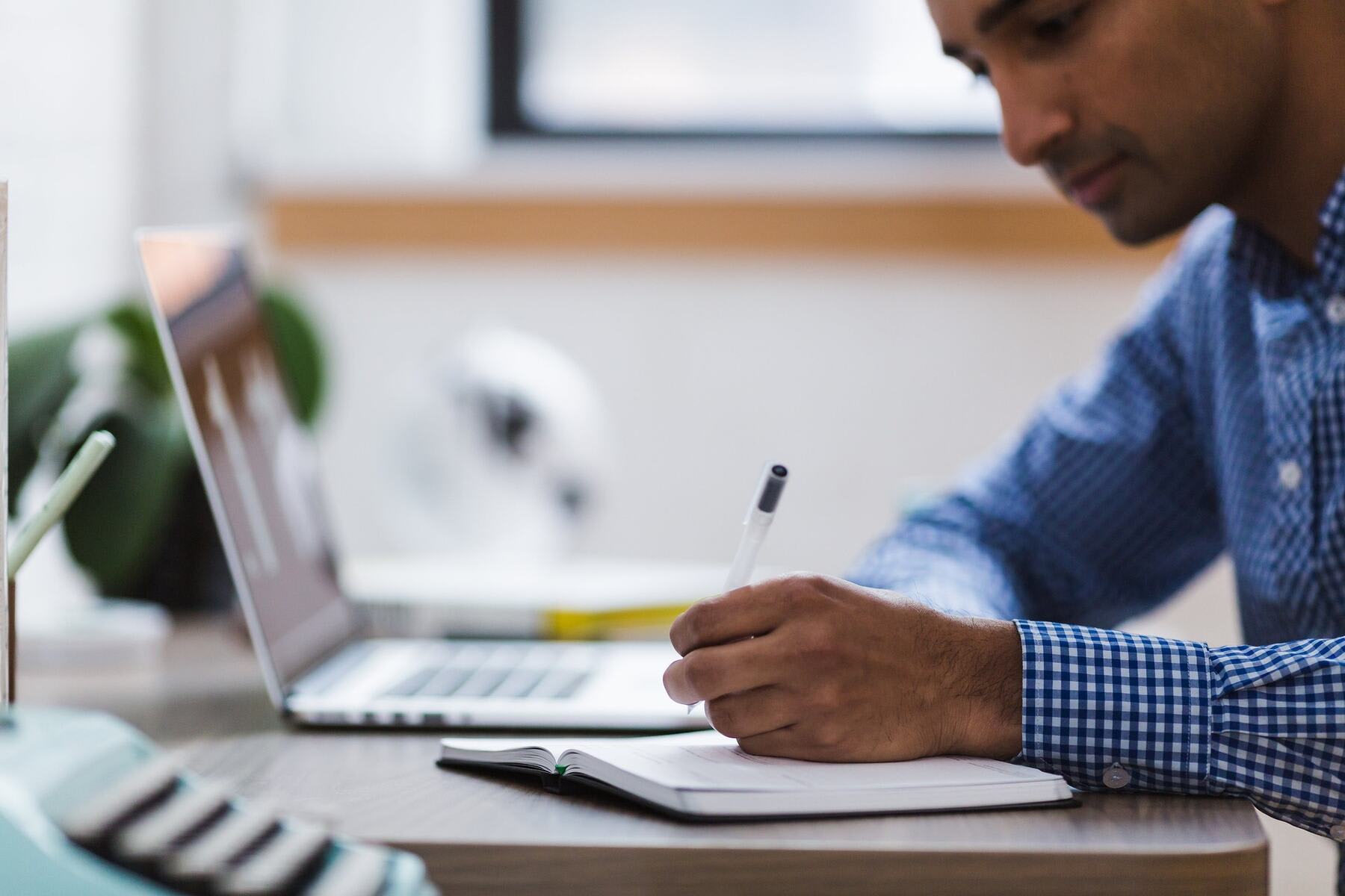 Man writing notes on his notebook with his laptop beside him