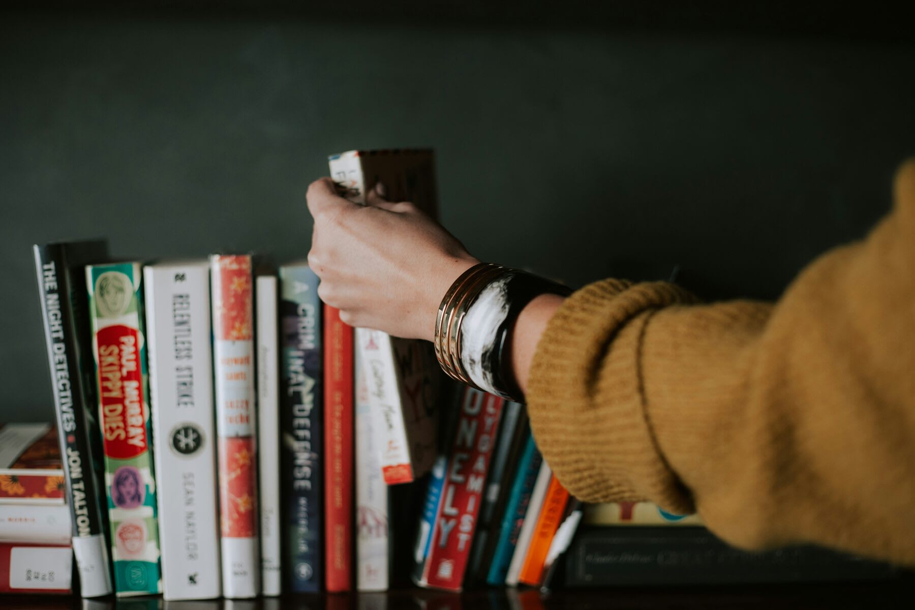 Person picking a book from a bookshelf