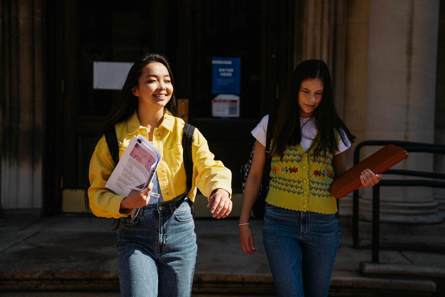 Two students holding folders while walking on campus grounds