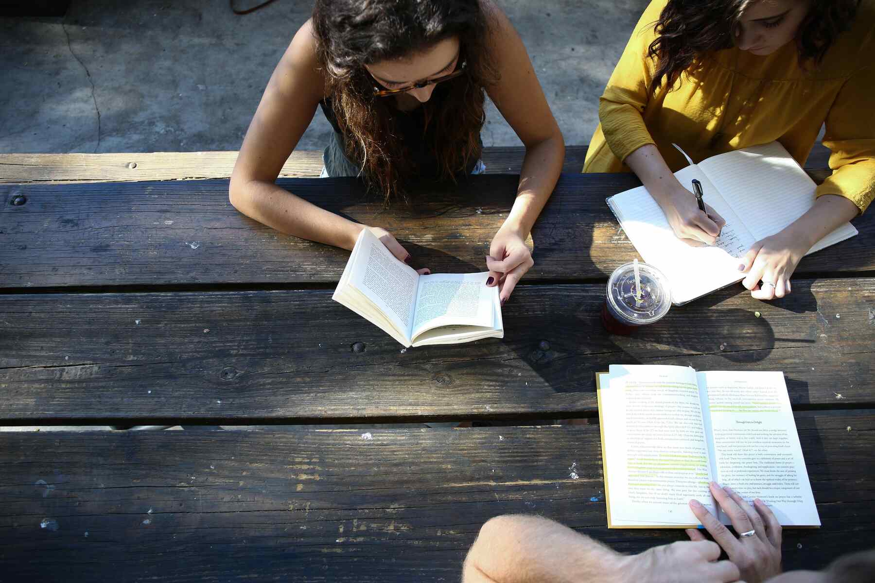 Three students reading and writing notes in an outdoor table