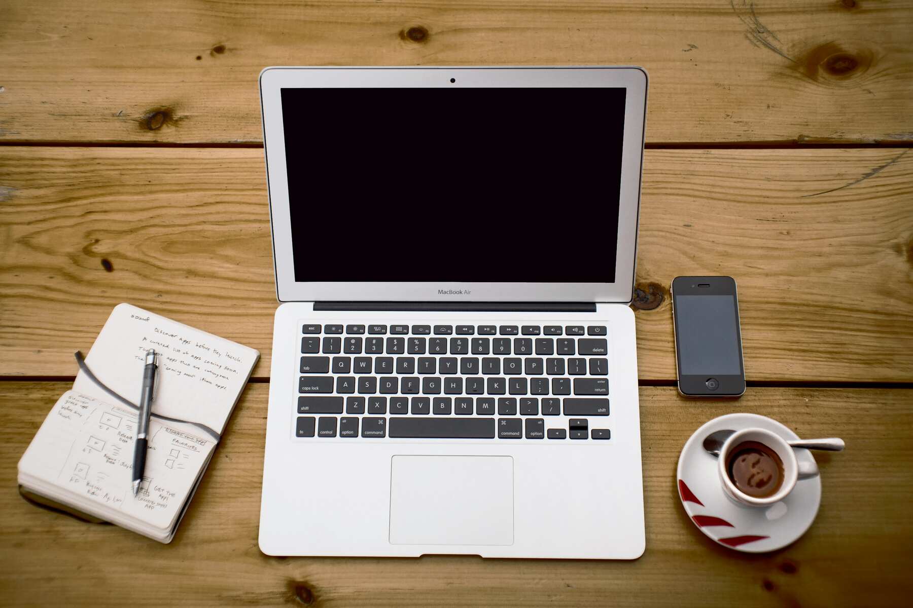 Laptop, smartphone, coffee mug, notebook and pen on a table