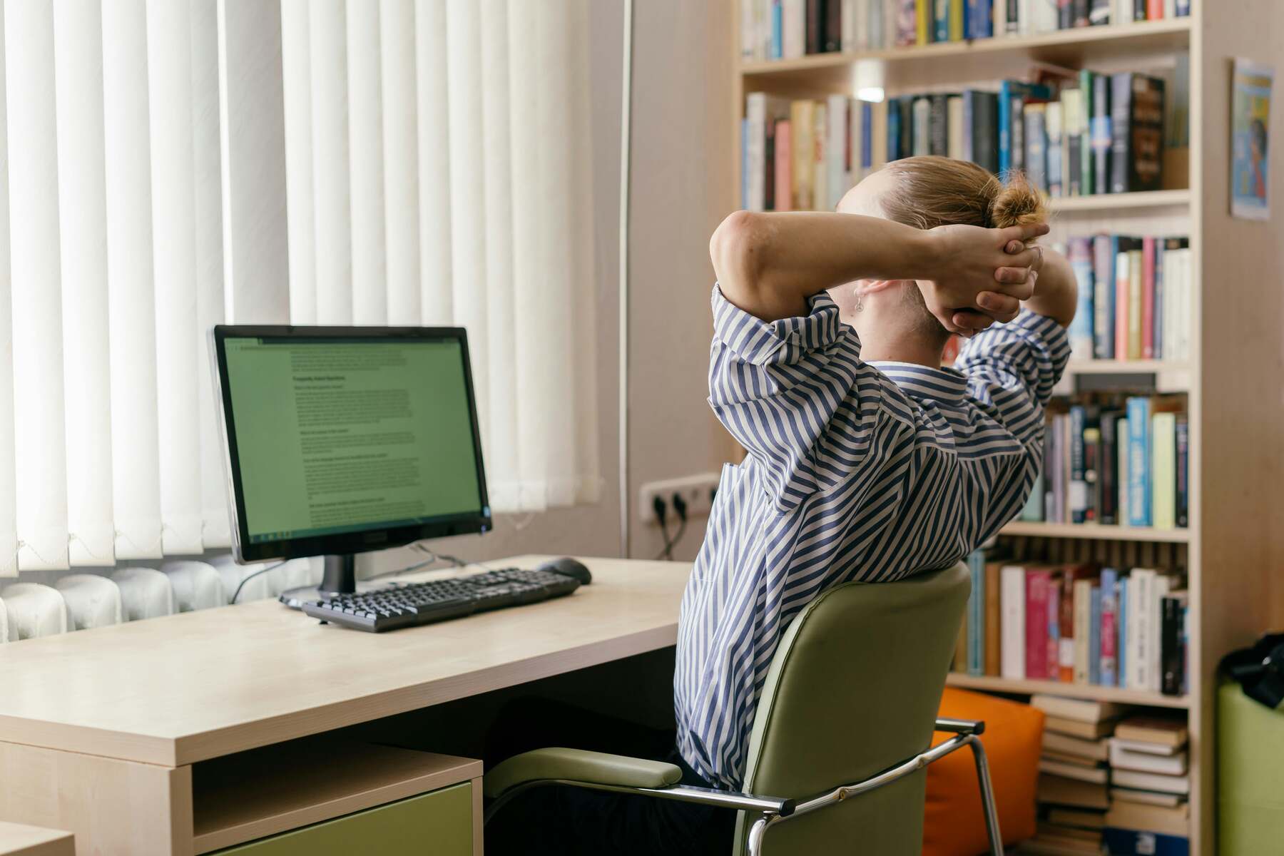 Woman looking at her desktop monitor with her hands behind the back of her head