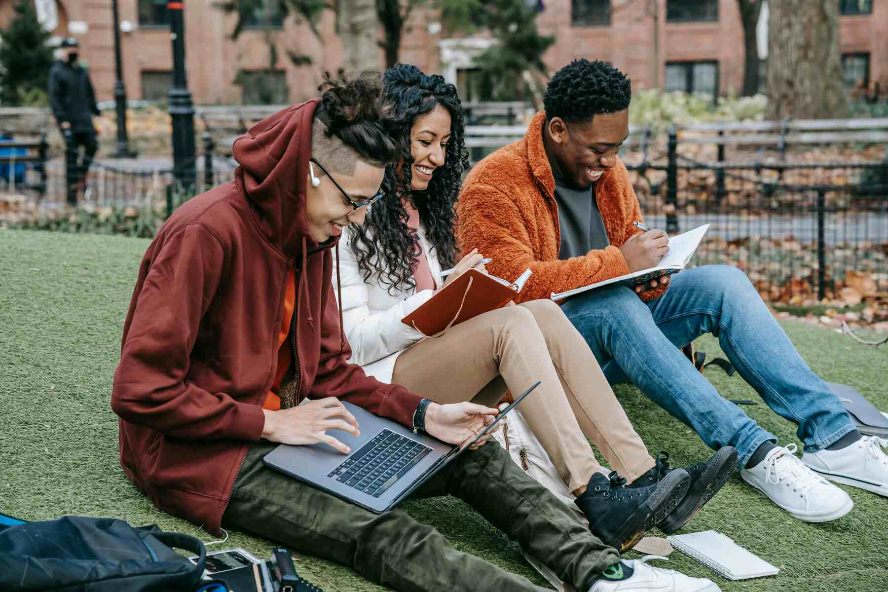 Three students sitting on the grass while studying with their laptop and notebooks