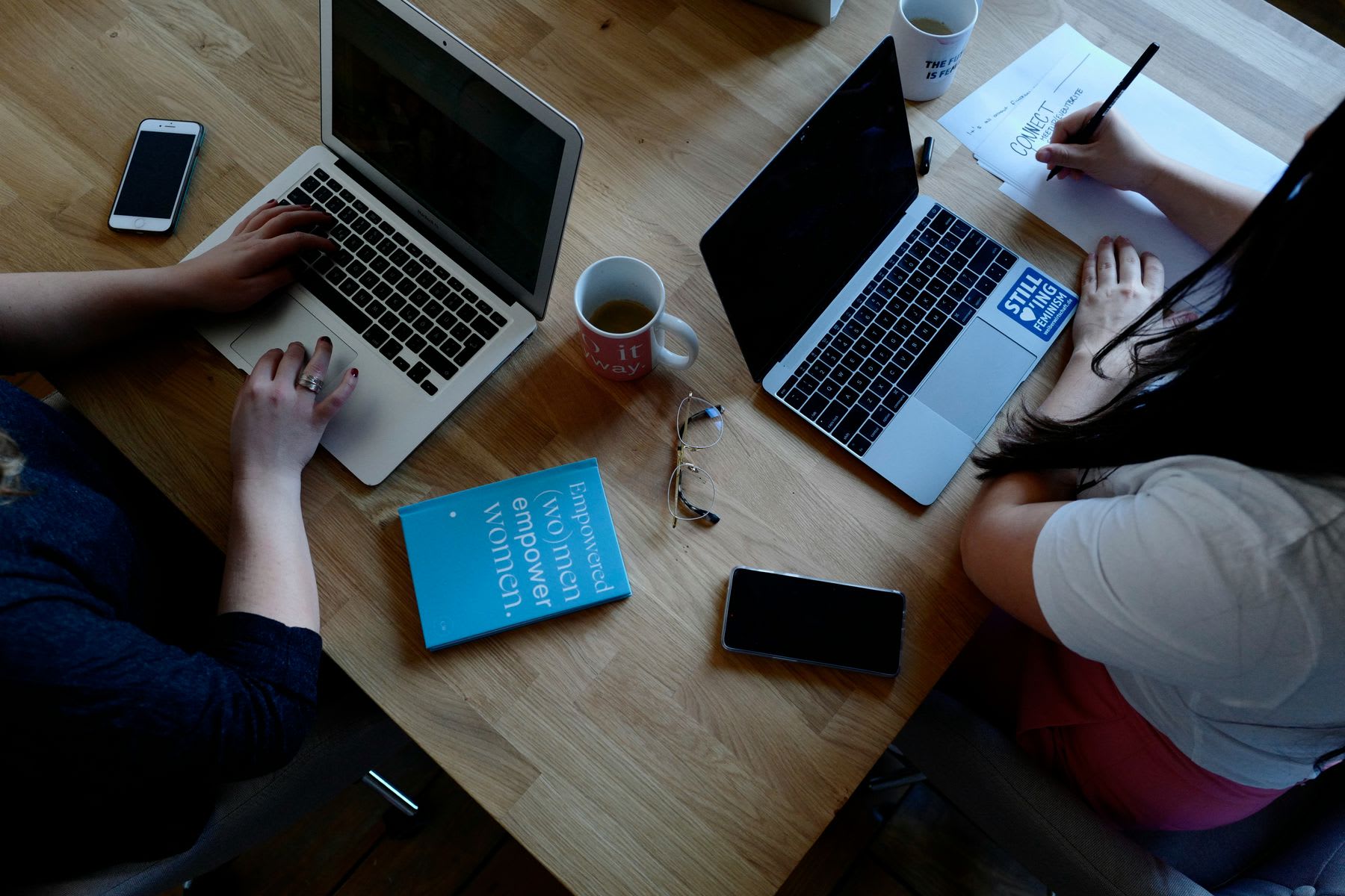 Two women sitting beside each other while studying and using their laptops