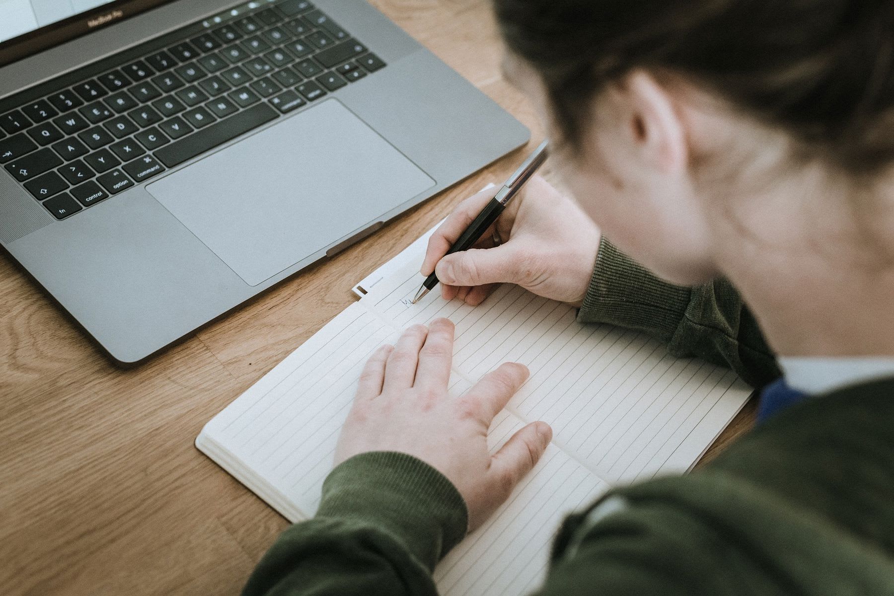 Woman writing notes while using her laptop