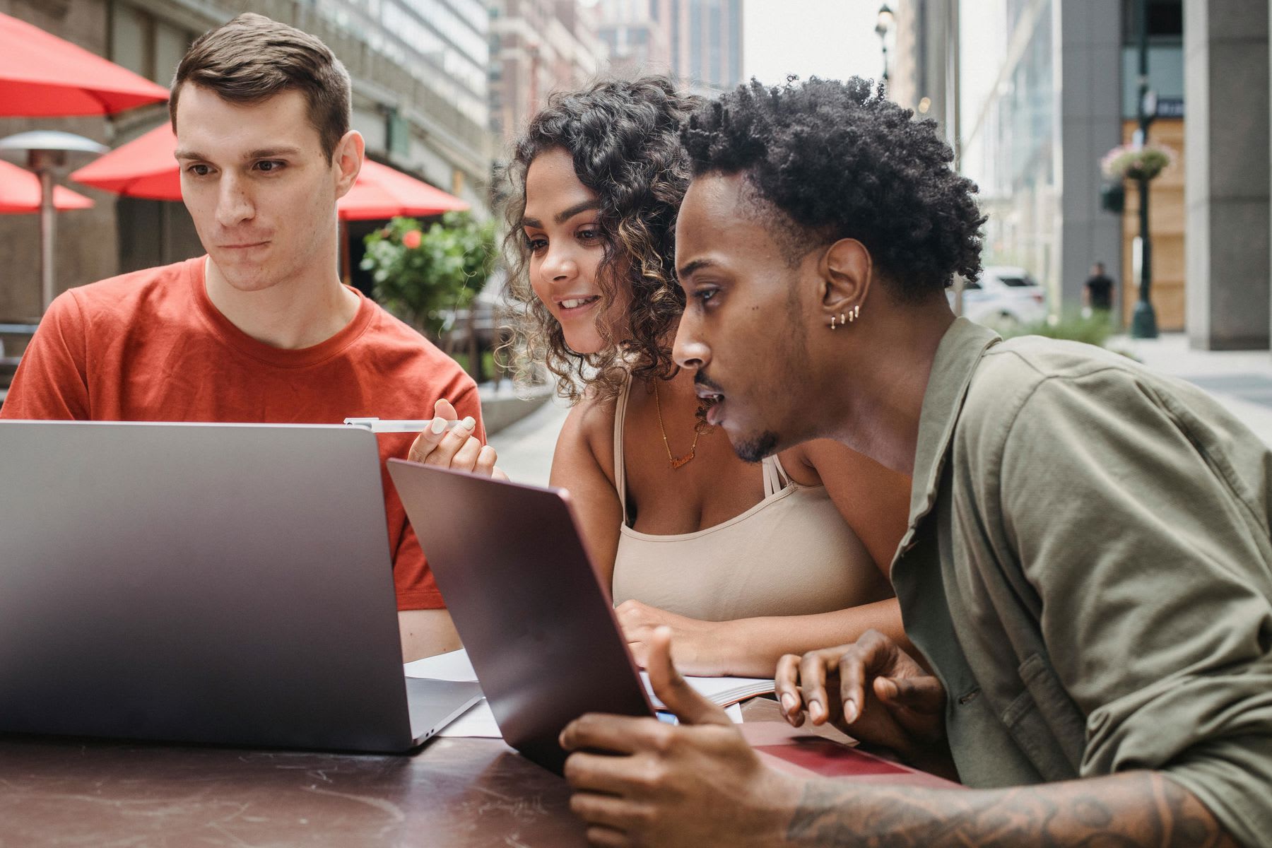 Students sitting on an outdoor cafe while looking at the same laptop screen during their study session