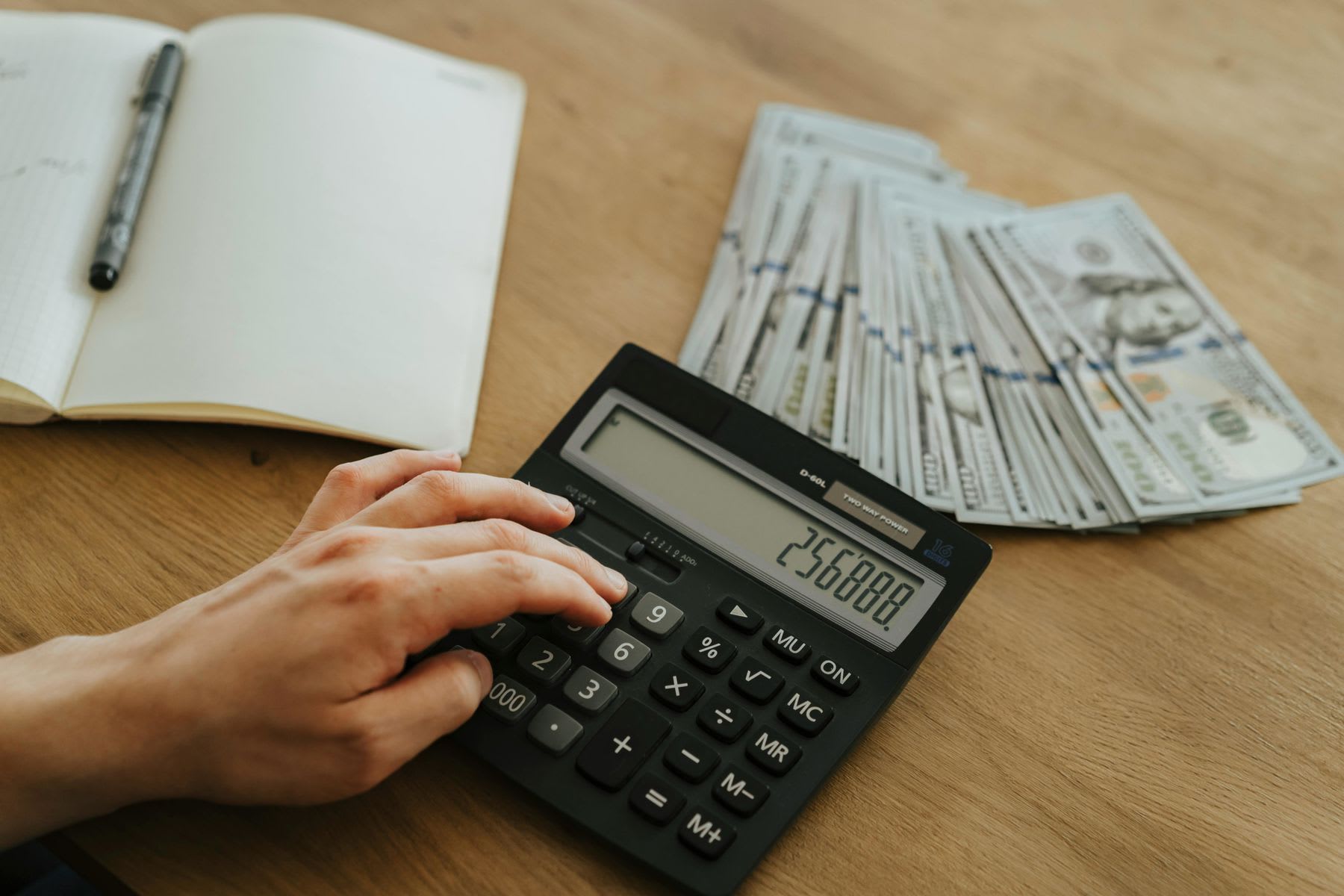 Person using a calculator while a pile of dollar bills are spread in the table