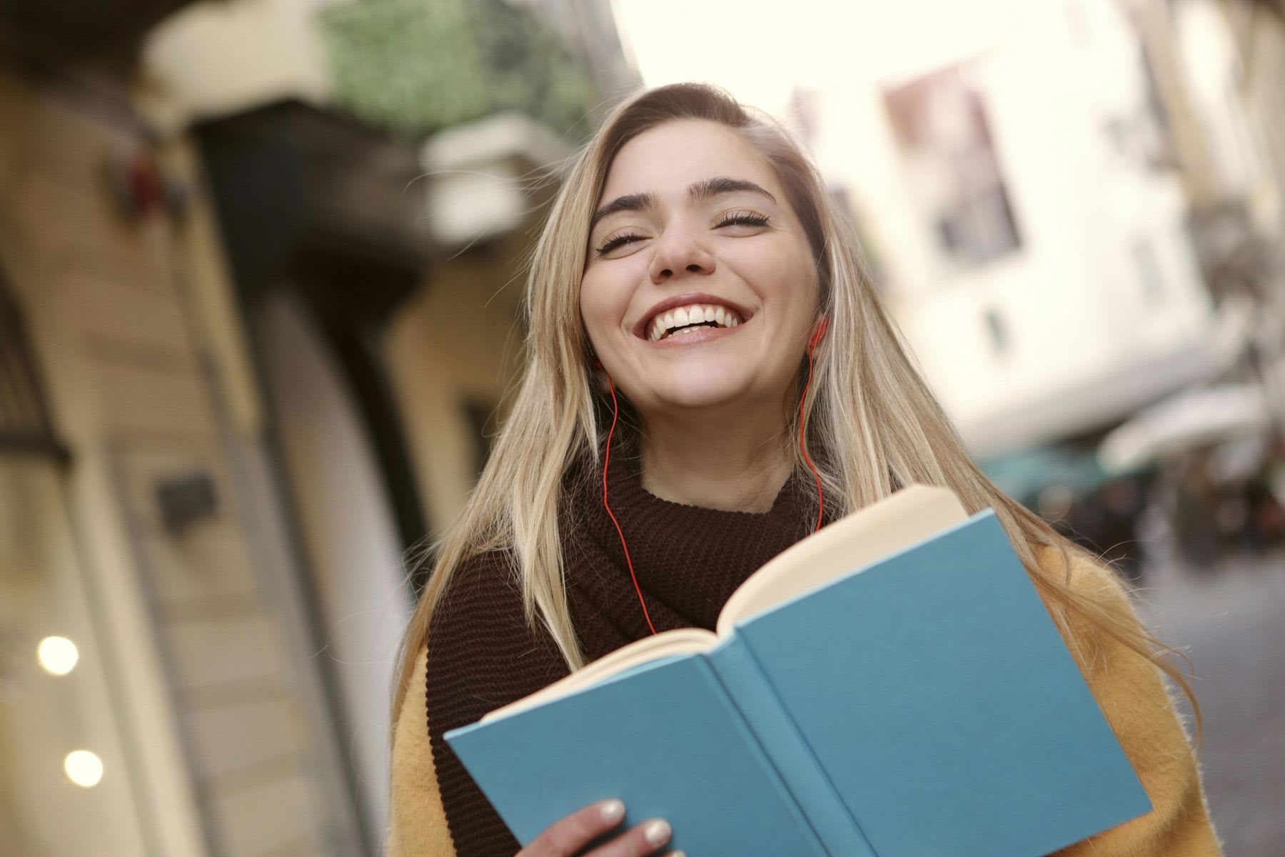 Woman smiling wide while listening to her earphones and holding a blue notebook