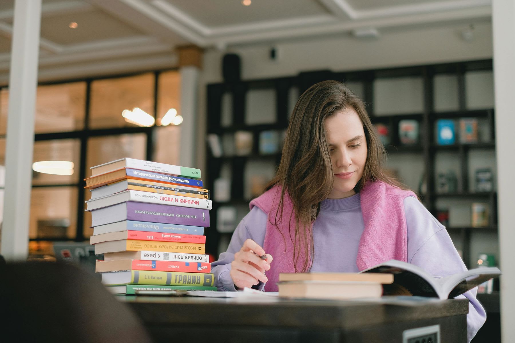 Woman writing notes while a pile of books are placed on her table