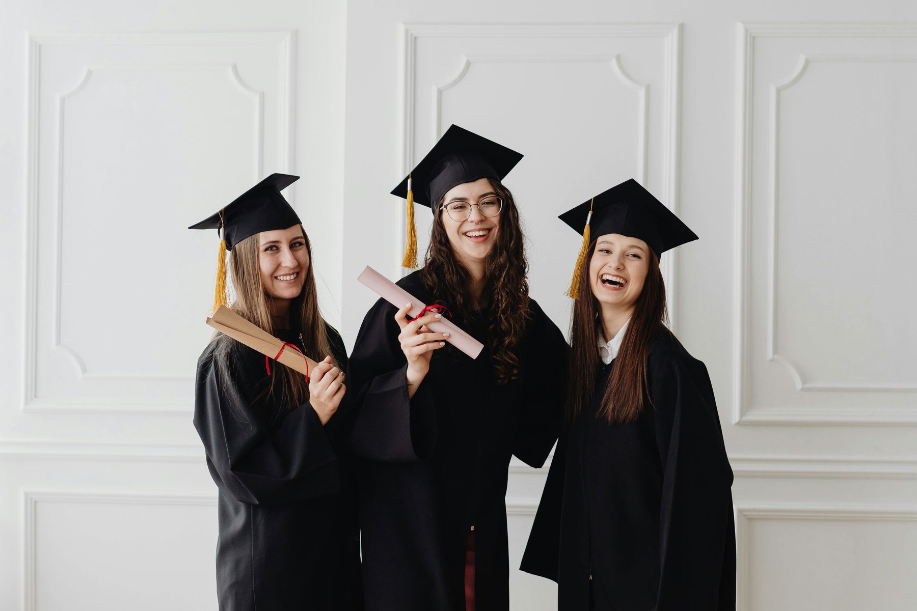 Three women wearing graduation caps and robes posing for their photos
