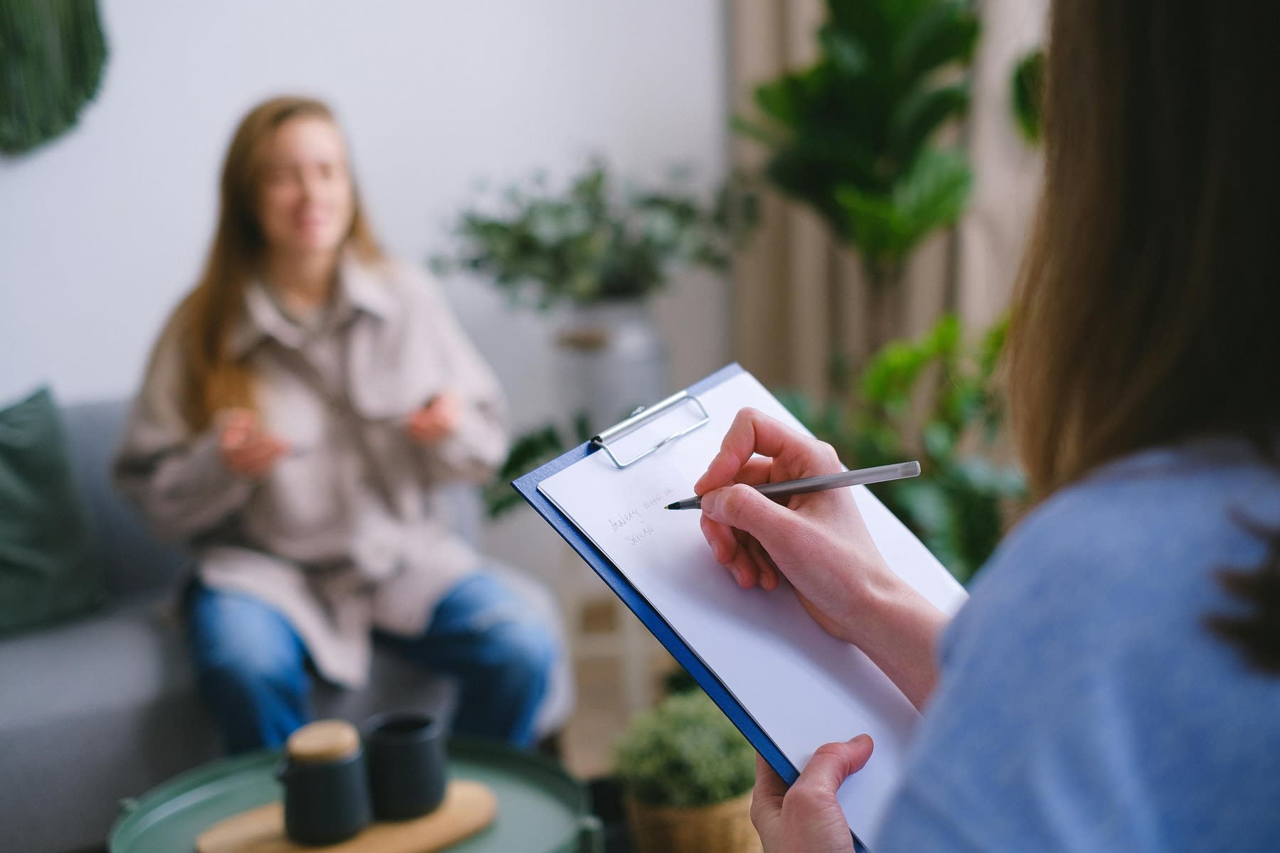 Woman writing down on her clipboard as a woman in her couch talks during a therapy session