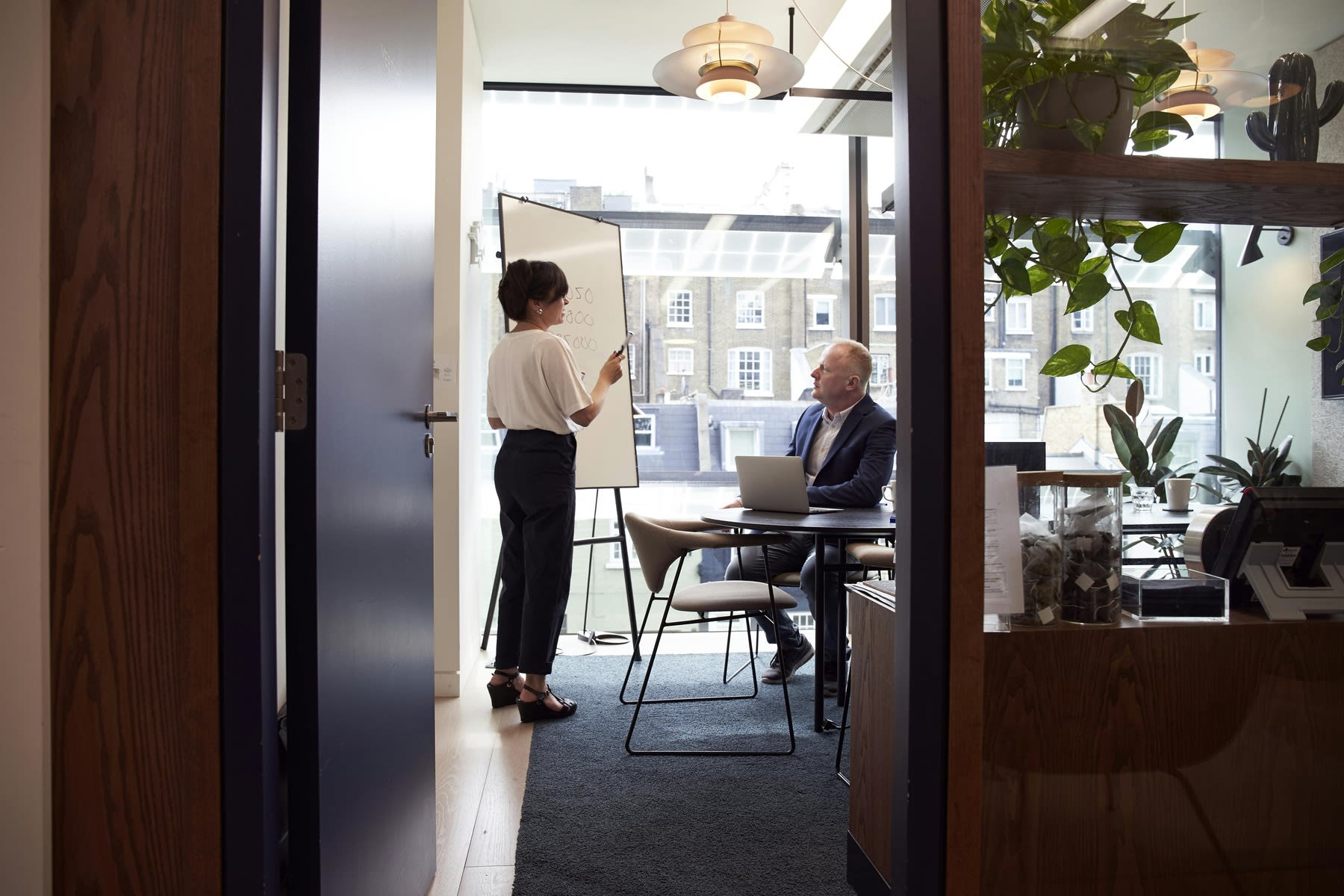 Woman explaining with the help of a whiteboard while a man listens intently, while sitting down