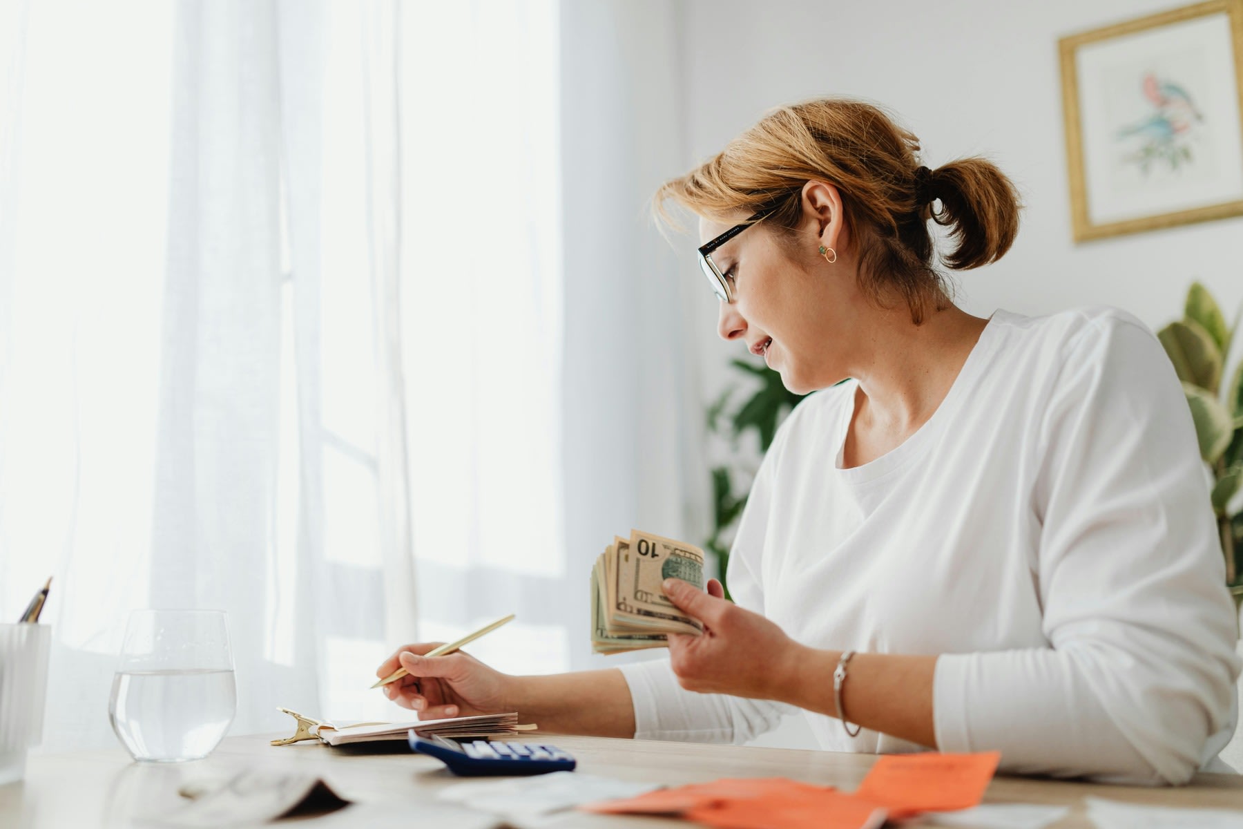 Woman holding dollar bills while writing notes on her notebook