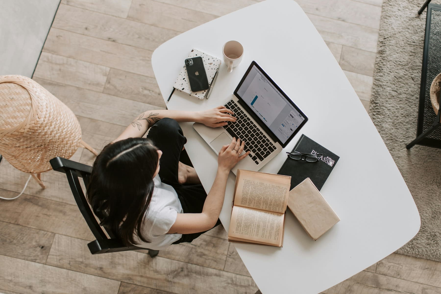 Overhead shot of a woman using her laptop while her books, notebook and phone are on the table