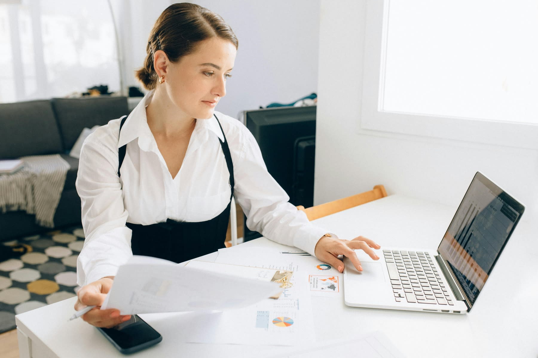 Woman holding a printed report while scrolling through her laptop