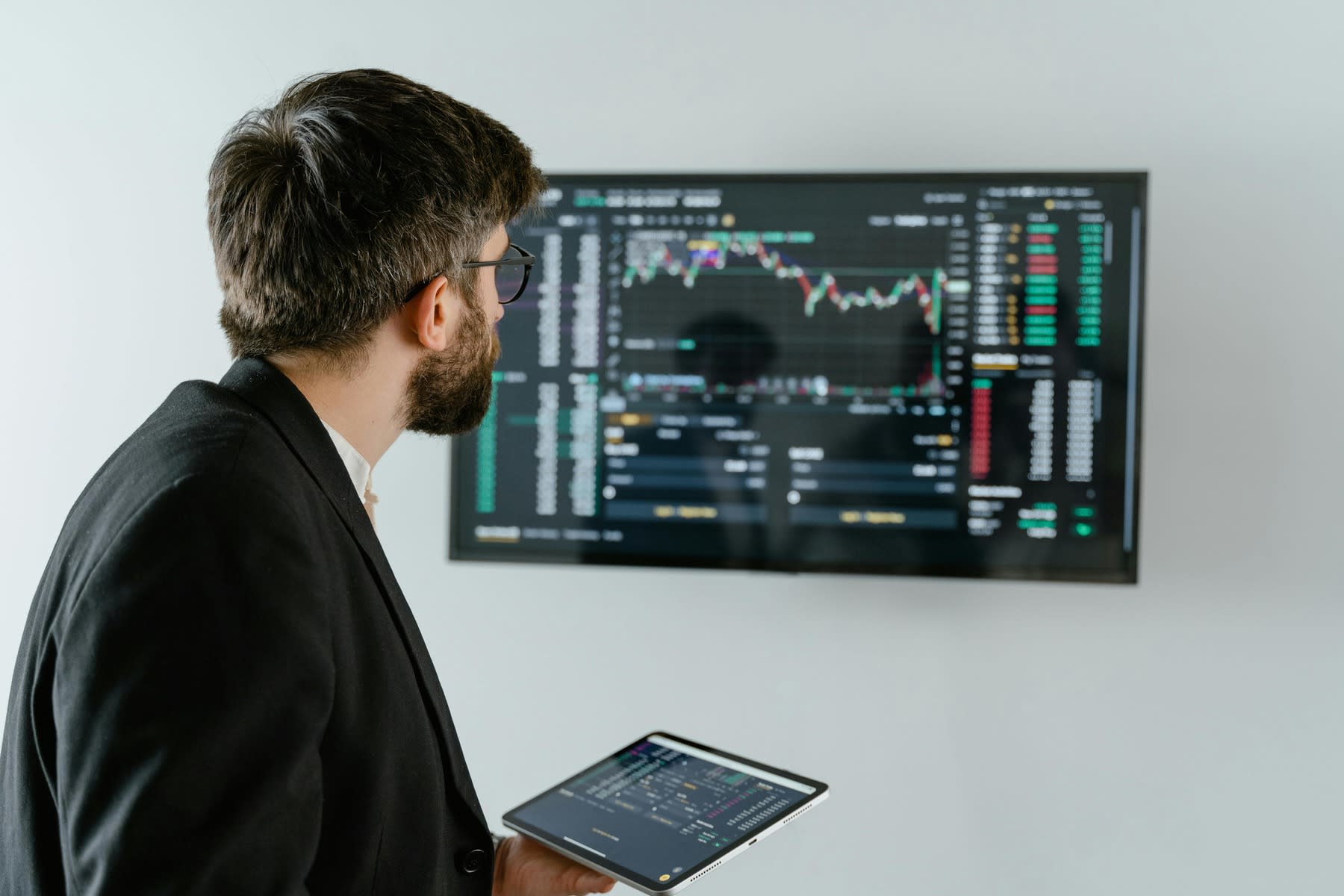 Man holding a tablet while looking at a monitor with data analytics data