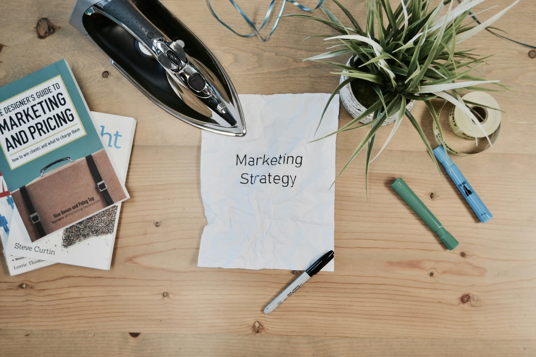 White paper with printed text of the word Marketing Strategy written on it, with books, pens and a pot of plant on the table