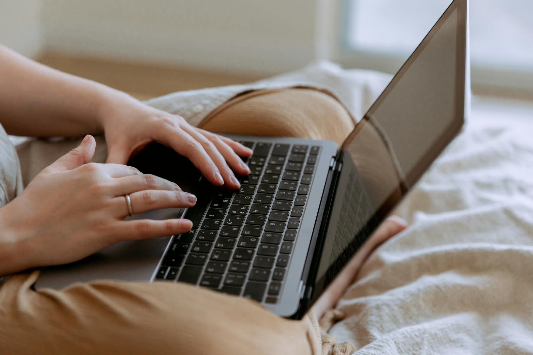Woman typing in her laptop while sitting on her bed