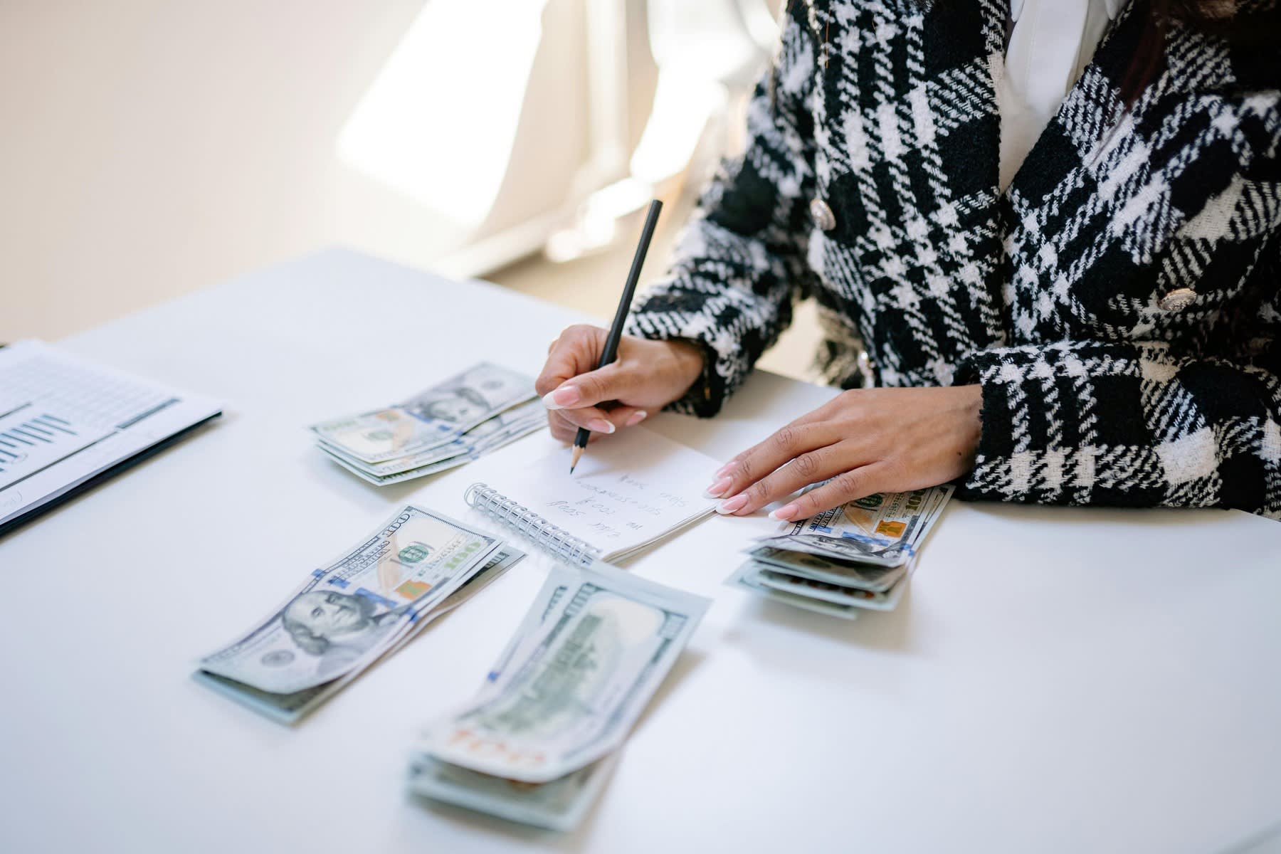 Woman writing notes, while dollar bills are stacked on the table